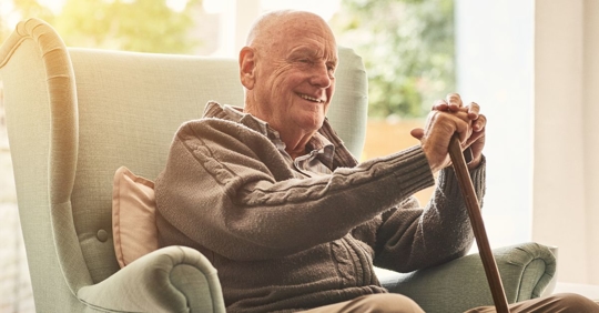 elderly man sitting in a recliner holding a walking cane and smiling