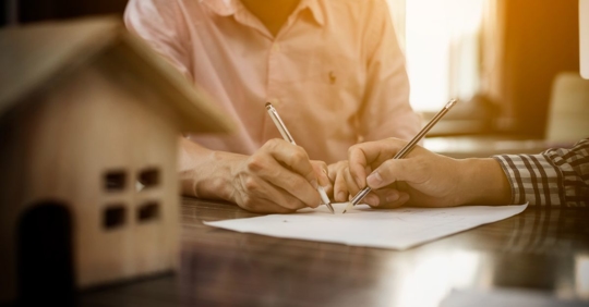 two people signing a contract with house figurine