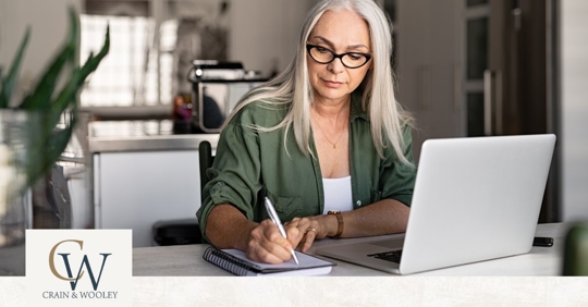 Older woman writing infront of laptop
